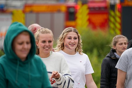 Personengruppe mit einer Person im Mittelpunkt, die eine dargestellte Verletzung im Gesicht hat