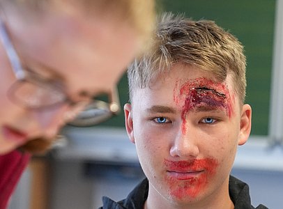 Einsatzkraft der DLRG beim Schminken einer weiteren Person mit einer Verletzung am Kopf