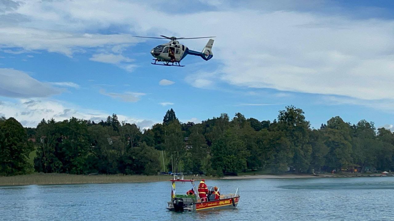 Auf dem Bild ist das mobile Motorrettungsboot „PELIKAN Gmund 99/3“ auf einem kgewässer und darüber fliegend ein Polizeihubschrauber zu sehen.